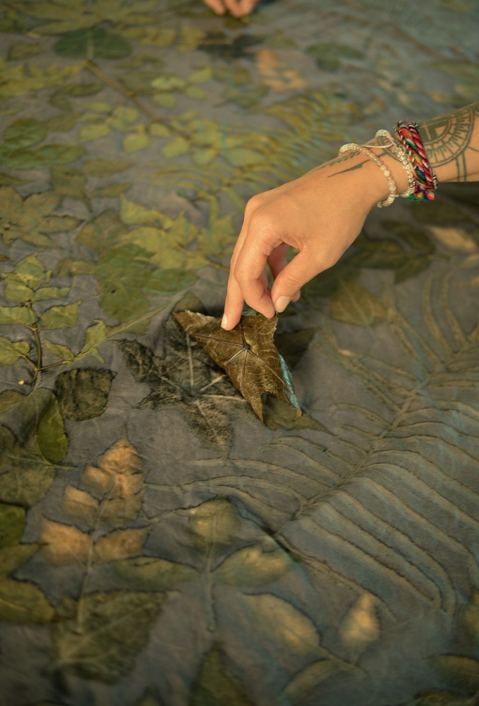 A hand lifting a leaf to reveal its impression on fabric